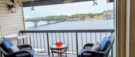 A balcony with wicker furniture, a small table, and a view of a river and bridge.