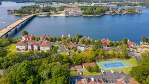 Vue aérienne d’un quartier résidentiel au bord d’un lac, avec un pont, un grand bâtiment doté d’un toit rouge et un court de tennis.