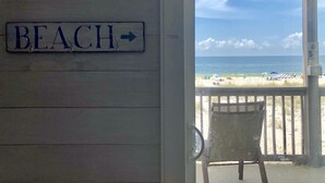 Uma porta de madeira com uma placa que diz 'BEACH' e vista para uma praia com guarda-sóis e pessoas.