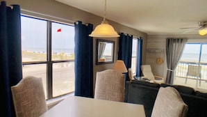 Um quarto com uma mesa, cadeiras, um sofá, uma luminária e vista para a praia.