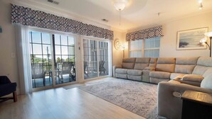 A spacious living room with a large sliding glass door leading to a balcony, a beige sofa, and a patterned rug. - Spacious Condo Close to Everything! -Pier Pleasure (Folly Beach)