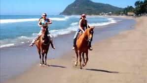 Deux personnes à cheval sur une plage, avec une montagne en arrière-plan.