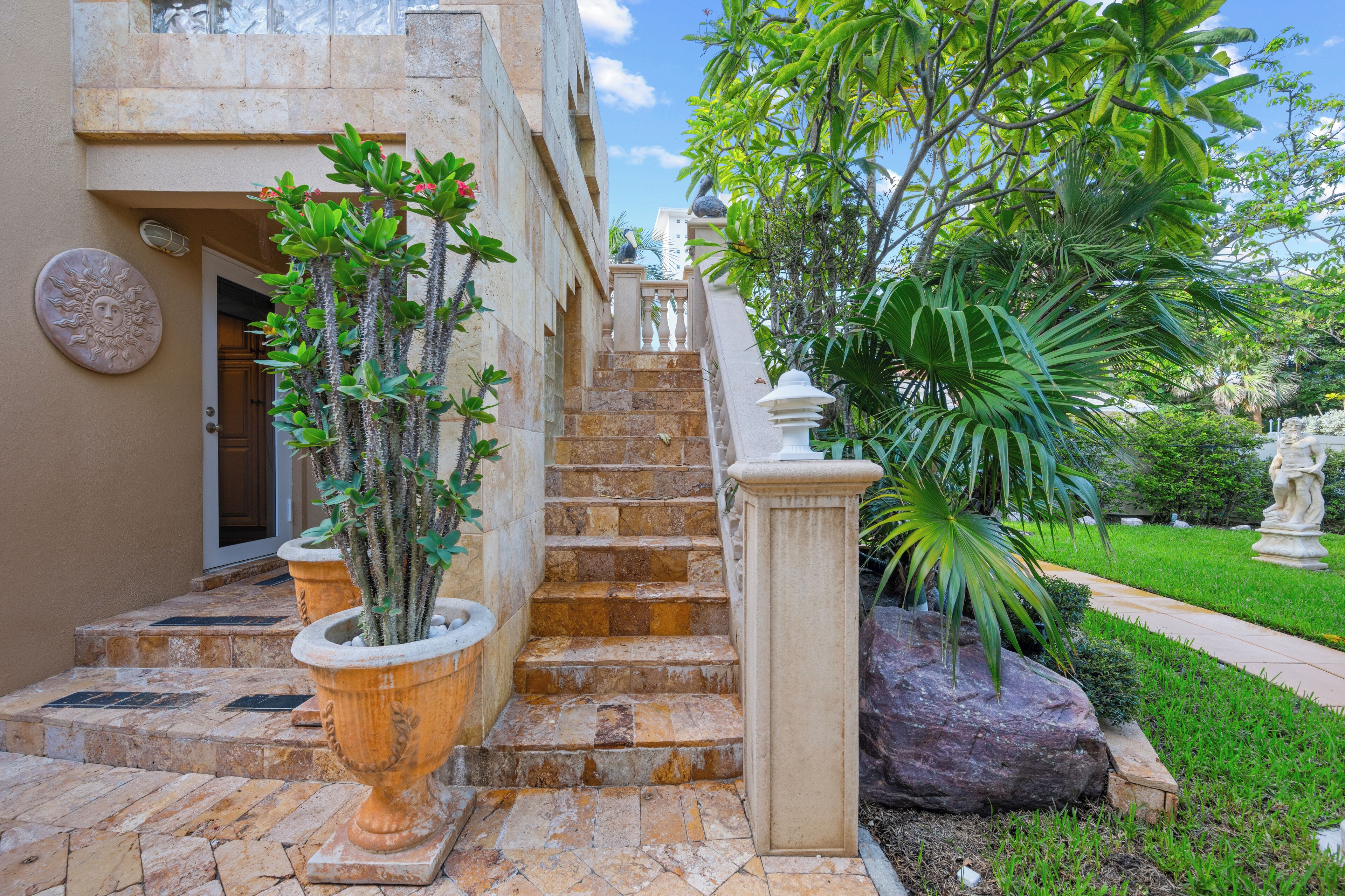 A staircase leading to a building entrance, flanked by potted plants and a statue.