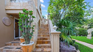 A staircase leading to a building entrance, flanked by potted plants and a statue.