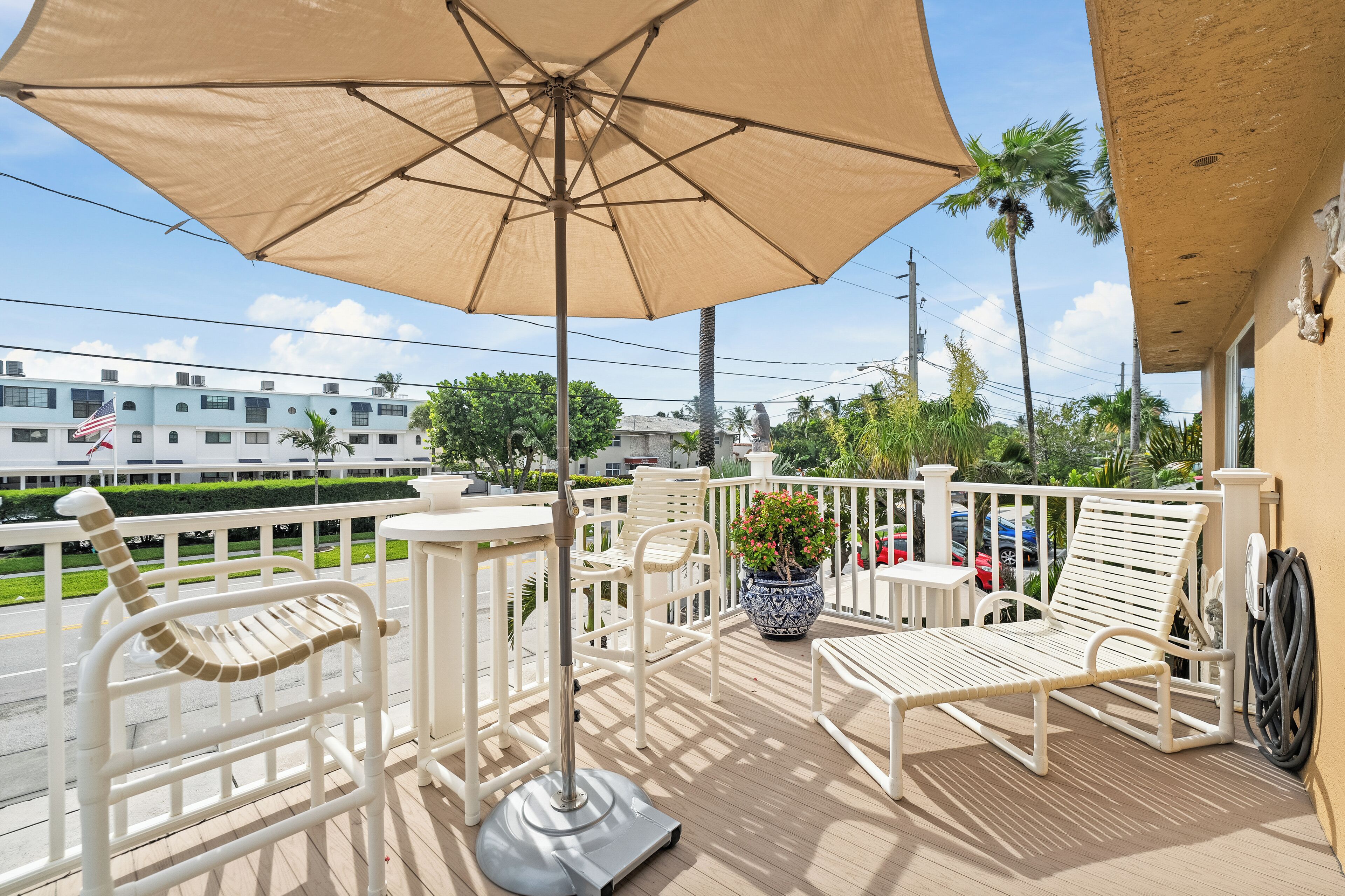 Een balkon met wit meubilair, waaronder stoelen en een tafel, en een grote beige parasol die schaduw biedt.