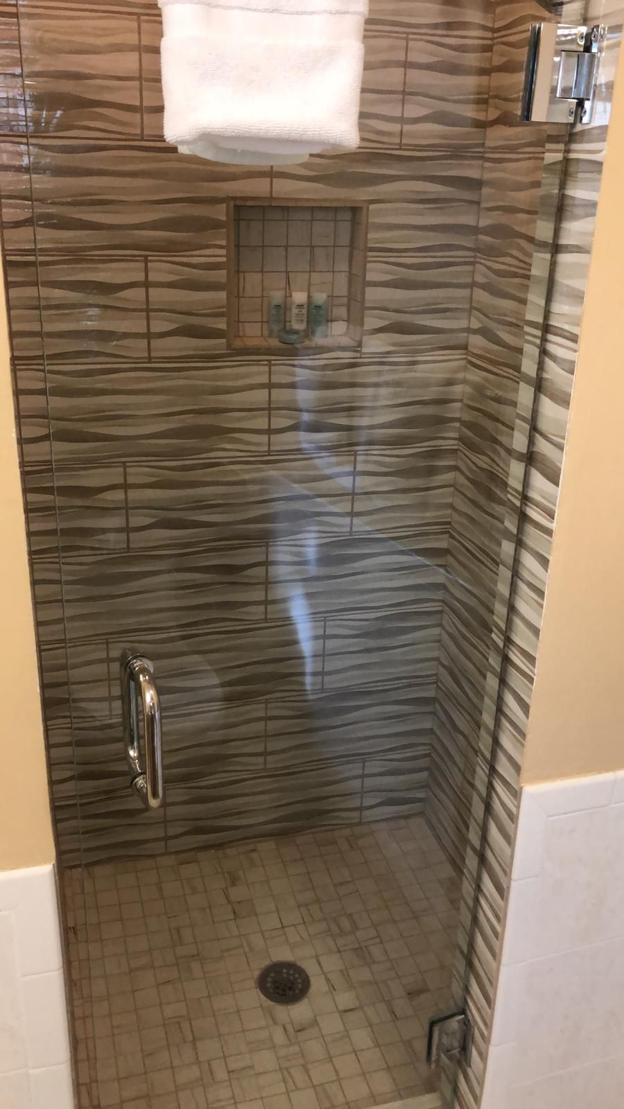 A shower with a tiled wall, a handrail, and a white towel hanging above.