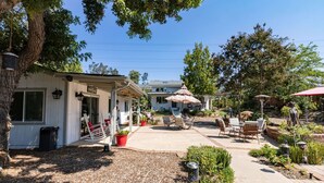 Un patio con mobiliario exterior, una zona de estar cubierta y un jardín con diversas plantas y un sendero.