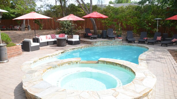 Un patio trasero con piscina, bañera de hidromasaje y mobiliario exterior.