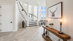 A spacious hallway with a wooden floor, a white door, a curved staircase, a console table with a lamp, and a framed picture on the wall. - 12 Collier Beach, Oceanfront, Pool, Great for Large Groups, Free Golf, Oceanfront (Hilton Head Island)
