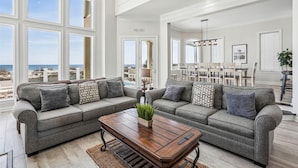 A spacious living room with a large gray sectional sofa, a wooden coffee table, and a view of the beach through large windows. - 12 Collier Beach, Oceanfront, Pool, Great for Large Groups, Free Golf, Oceanfront (Hilton Head Island)