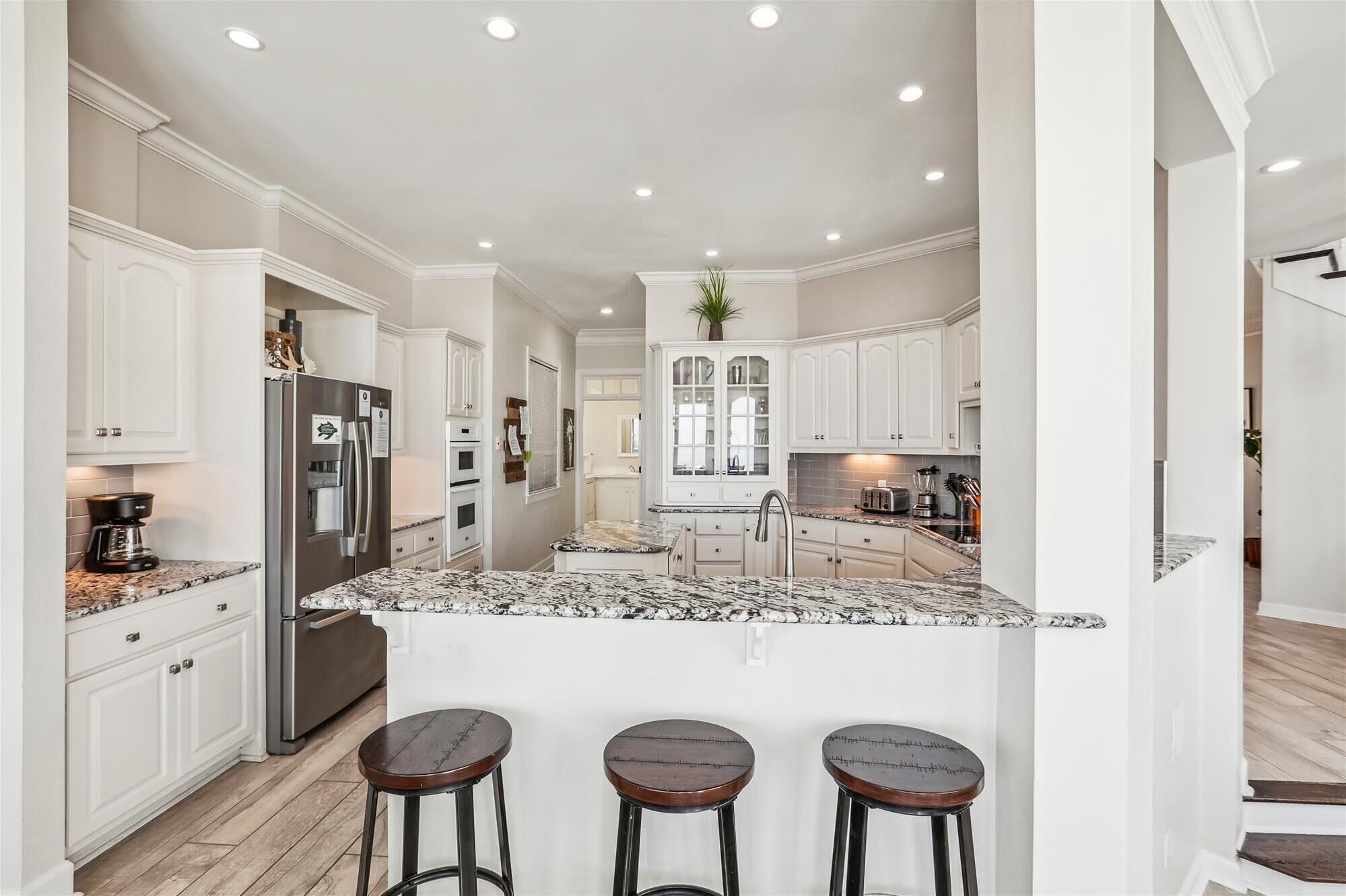 A spacious kitchen with white cabinetry, a granite countertop, and a central island with bar stools.