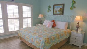 A bedroom with a bed, two bedside tables, a window with blinds, and a painting on the wall. - Luxury Beachfront Home with Extra Large Deck;  Sleeps up to 20! (Gulf Shores)