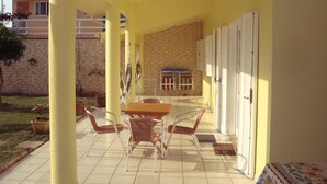 Een terras buiten met een tafel en stoelen, een bakstenen muur en een overdekt gedeelte met een deur.