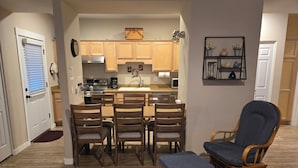 A compact kitchen with wooden cabinets, a dining area with chairs, and a small seating area with a chair and ottoman.