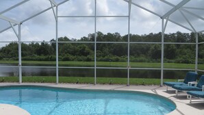 A covered swimming pool with lounge chairs, a view of a lake, and a grassy area. - 5 BR/4 BA/2-Floors/Keyless Entry/Contactless Check-In/1-Day Between Rentals/WiFi (Kissimmee)