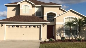 A two-story house with a garage, a front door, and a small porch with plants. - 5 BR/4 BA/2-Floors/Keyless Entry/Contactless Check-In/1-Day Between Rentals/WiFi (Kissimmee)