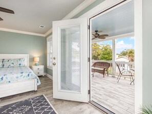 Un dormitorio con cama, mesita de noche y vistas a un patio exterior con sillas y ventilador de techo.