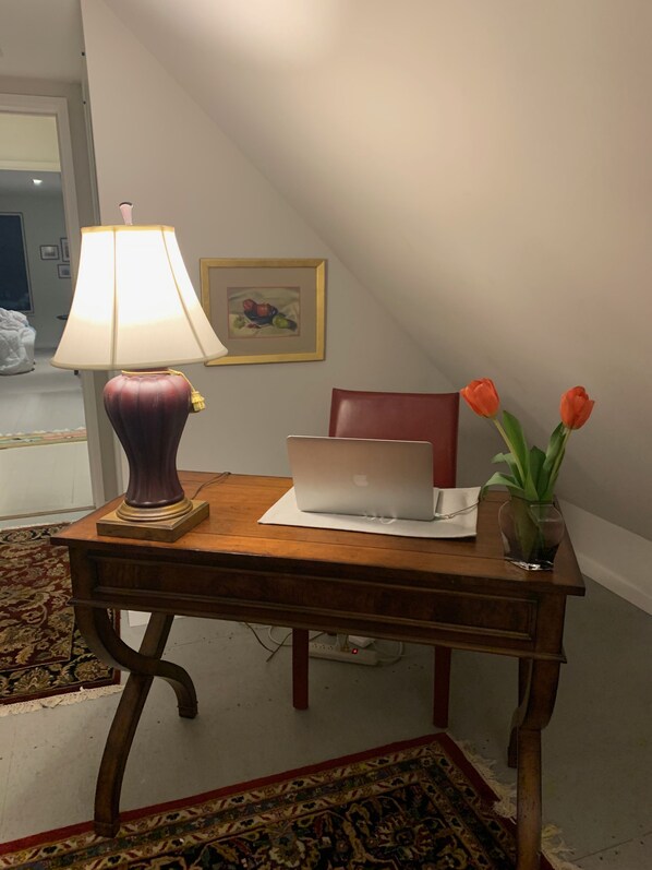 Un escritorio de madera con una computadora portátil, una lámpara y un florero con flores.