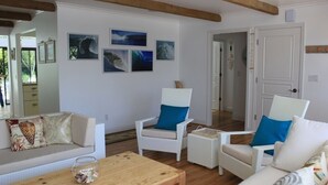 Un salon avec un canapé blanc, deux fauteuils en osier blanc dotés de coussins bleus, une table basse en bois et un bocal en verre contenant des poissons.