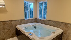 A modern bathroom with a large hot tub, two windows with a view of trees, and a built-in control panel.