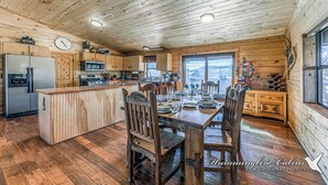 Cocina de cabaña de madera con una isla central, armarios de madera, un refrigerador, microondas y una mesa de comedor para cuatro.