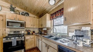 Una cocina compacta con armarios de madera, estufa, microondas, lavamanos y cafetera.