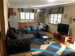 Ein Wohnzimmer mit einer Couch, einem Couchtisch, einem Fernseher und einer Küche im Hintergrund.