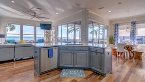 Une cuisine moderne dotée d’un grand îlot central, d’appareils électroménagers intégrés et offrant une vue sur l’océan.
