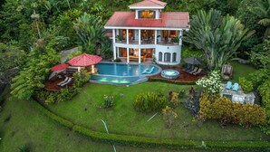 Une maison à deux étages avec une piscine, entourée d’une végétation luxuriante.