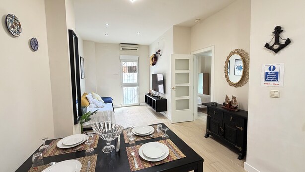 A dining area with a table set for four, a TV in the background, and a 'Quiet please people sleeping' sign on the wall. - ⭐️Best XL Valencia Beach Flat♜ Historic Area♜Beach (Valencia)