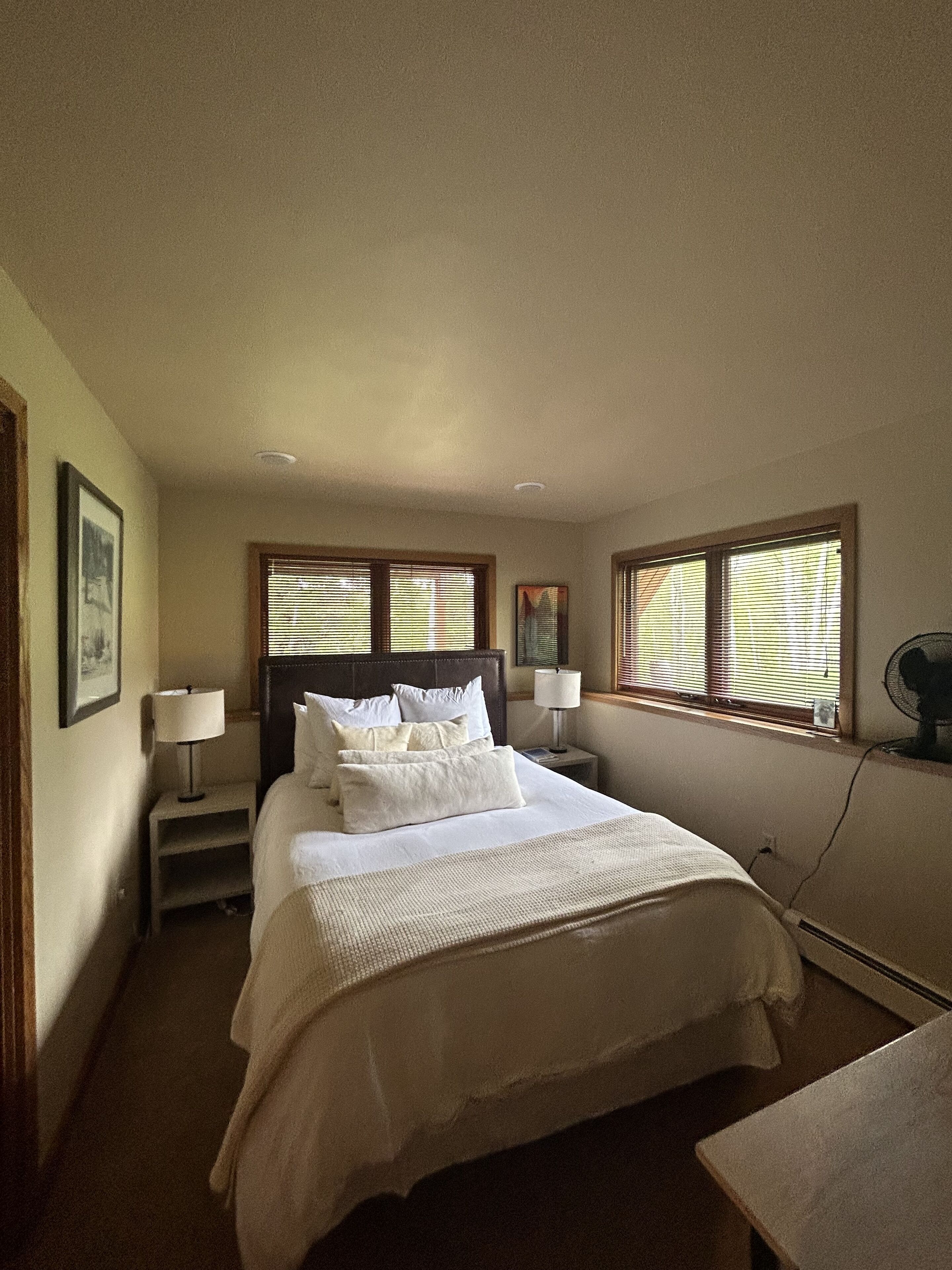 Un dormitorio ordenado con una cama grande, dos mesitas de noche con lámparas y una ventana con persianas.