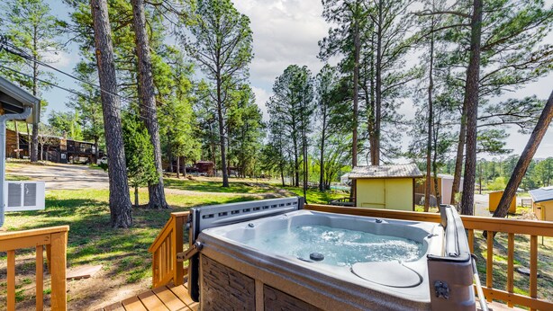 A hot tub on a wooden deck surrounded by trees, with a view of a residential area in the background. - Happy Days Inn | Your Happy Place in the Pines w/ Hot Tub,Views & Pet Friendly (Ruidoso)