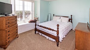 A bedroom with a wooden bed, a dresser, a television on a stand, and a window with a view of palm trees. - Gorgeous Oceanfront 3Bedroom Away From The Hustle and Bustle (St Augustine)