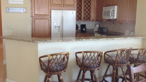 A kitchen with wooden cabinets, a refrigerator, a microwave, and a coffee maker. There are four wicker chairs in front of the counter. - Gorgeous Oceanfront 3Bedroom Away From The Hustle and Bustle (St Augustine)