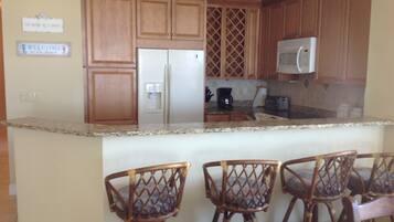 A kitchen with wooden cabinets, a refrigerator, a microwave, and a coffee maker. There are four wicker chairs in front of the counter.