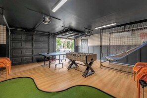 Une pièce équipée d’une table de ping-pong, d’un baby-foot et d’un espace délimité par un filet, probablement destiné à la pratique de sports.