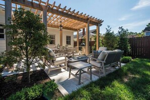 Une terrasse couverte, aménagée avec du mobilier d’extérieur, une pergola et un petit arbre.