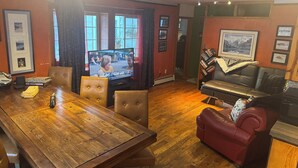 Ett vardagsrum med ett matbord i trä, läderstolar, en tv och en röd lädersoffa.