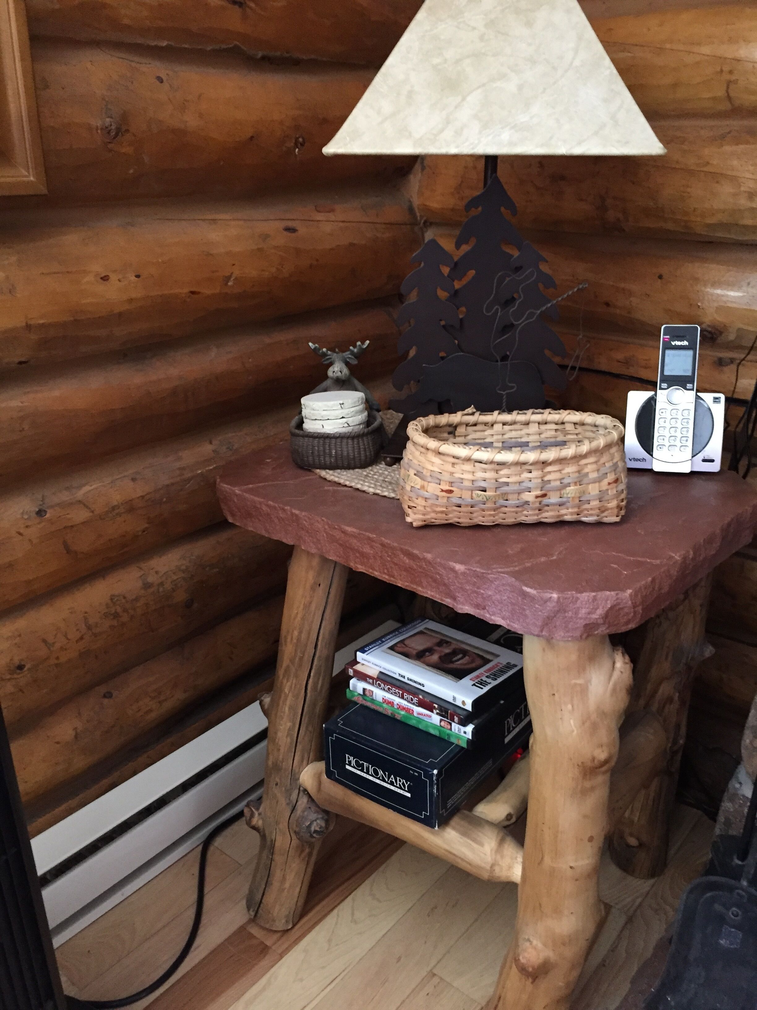 A wooden table with a lamp, a woven basket, a stack of books, and a phone.