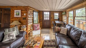 A log cabin interior with a fireplace, leather sofas, a dining table, and a view of the outdoors.