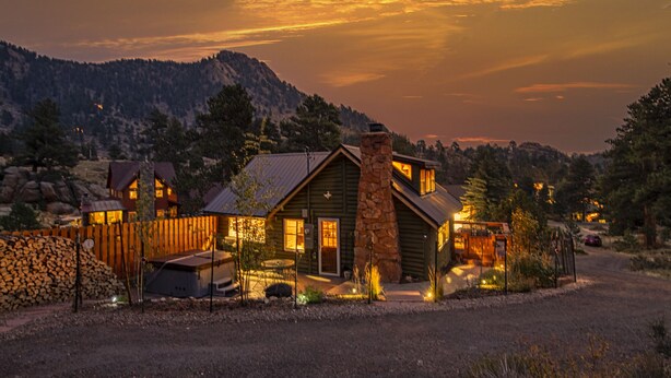 A rustic cabin with multiple rooms, a stone chimney, and a wooden fence.