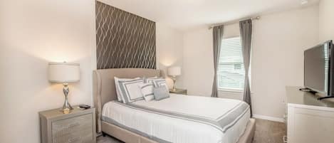 A bedroom with a bed, bedside tables, a television, and a window with curtains.