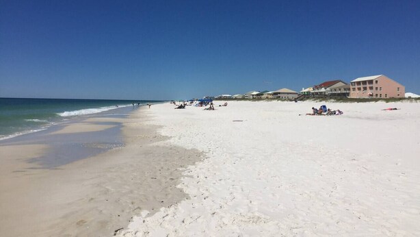 Ein Strand mit weißem Sand, blauem Himmel und einigen Gebäuden im Hintergrund.