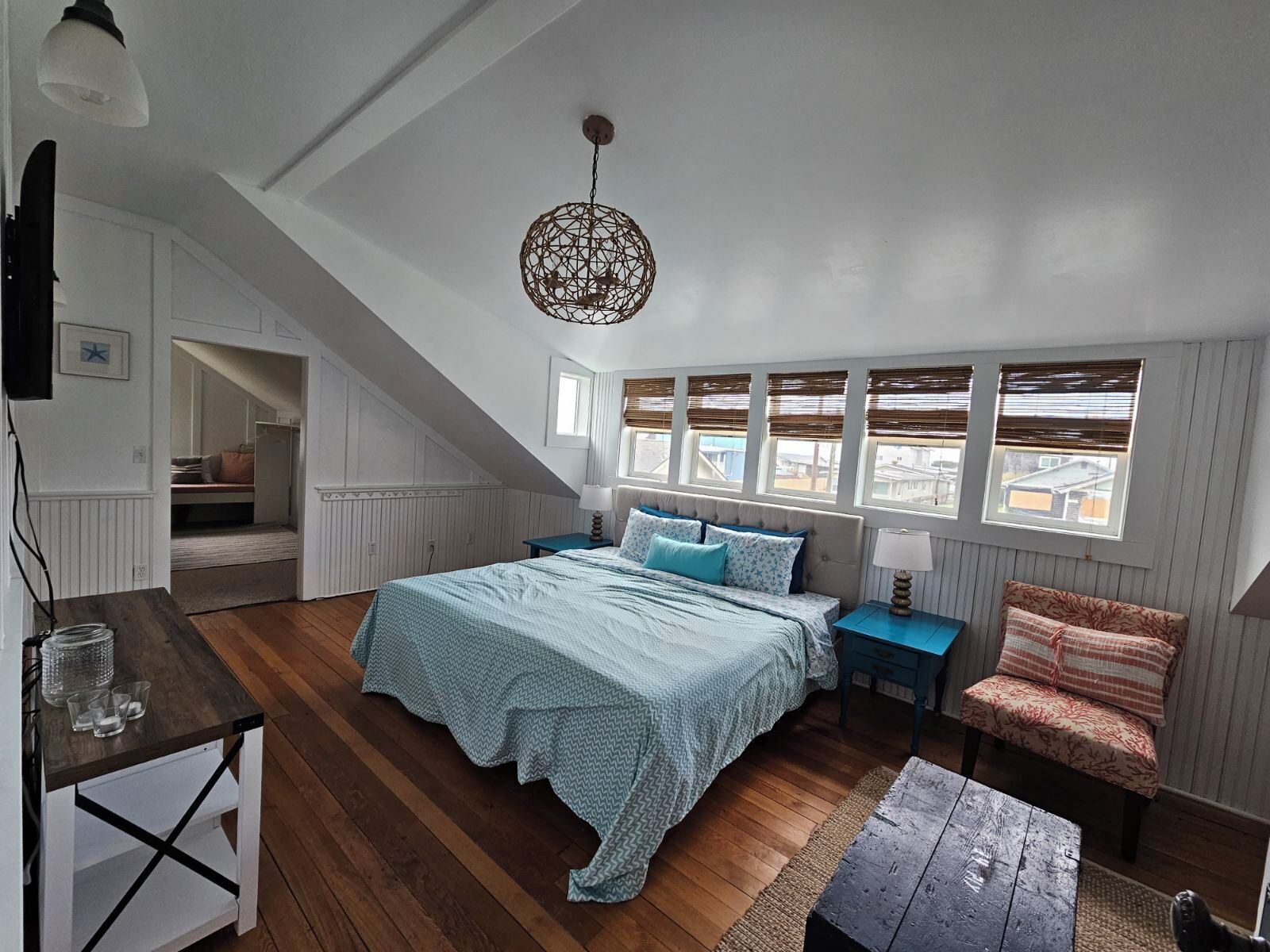 A bedroom with a sloped ceiling, a bed with a patterned bedspread, a nightstand, a chair, and a wooden table.
