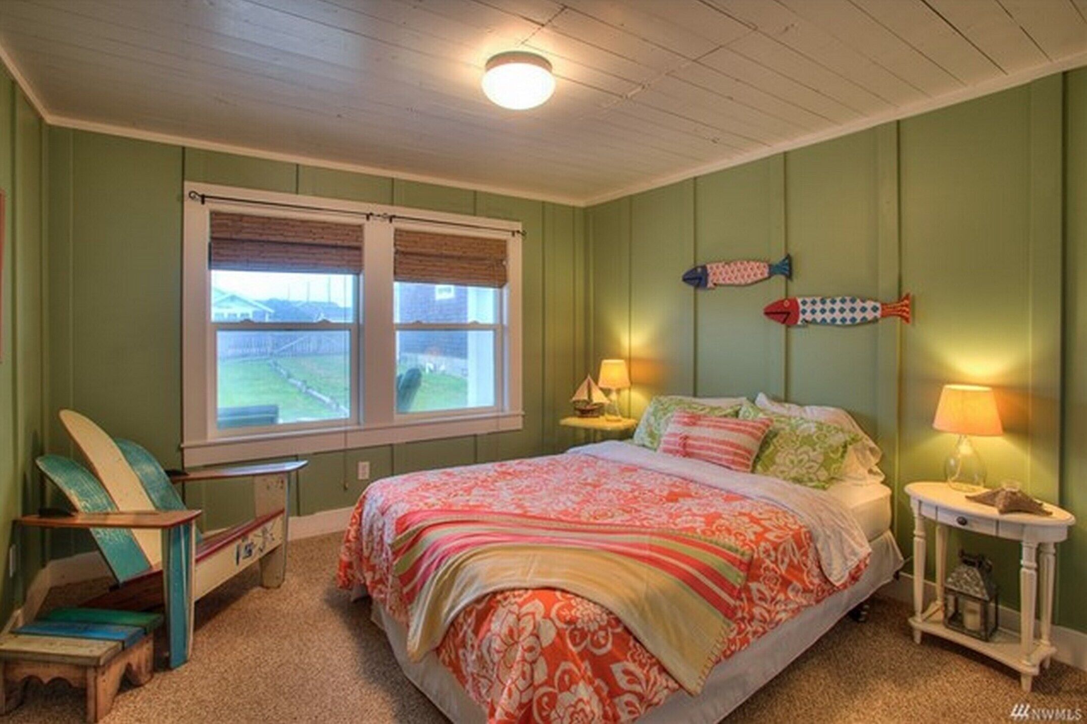 Un dormitorio con una cama, dos mesitas de noche, una silla, una ventana y una decoración de peces en la pared.
