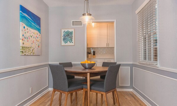 Een eetgedeelte met een ronde houten tafel, vier stoffeerde grijze stoelen, een fruitschaal en een hanglamp.