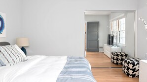 Ett modernt sovrum med en säng, ett sängbord, en lampa och en stor spegel.