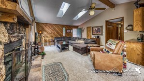 A spacious living room with a stone fireplace, a large sectional sofa, and a ceiling fan.