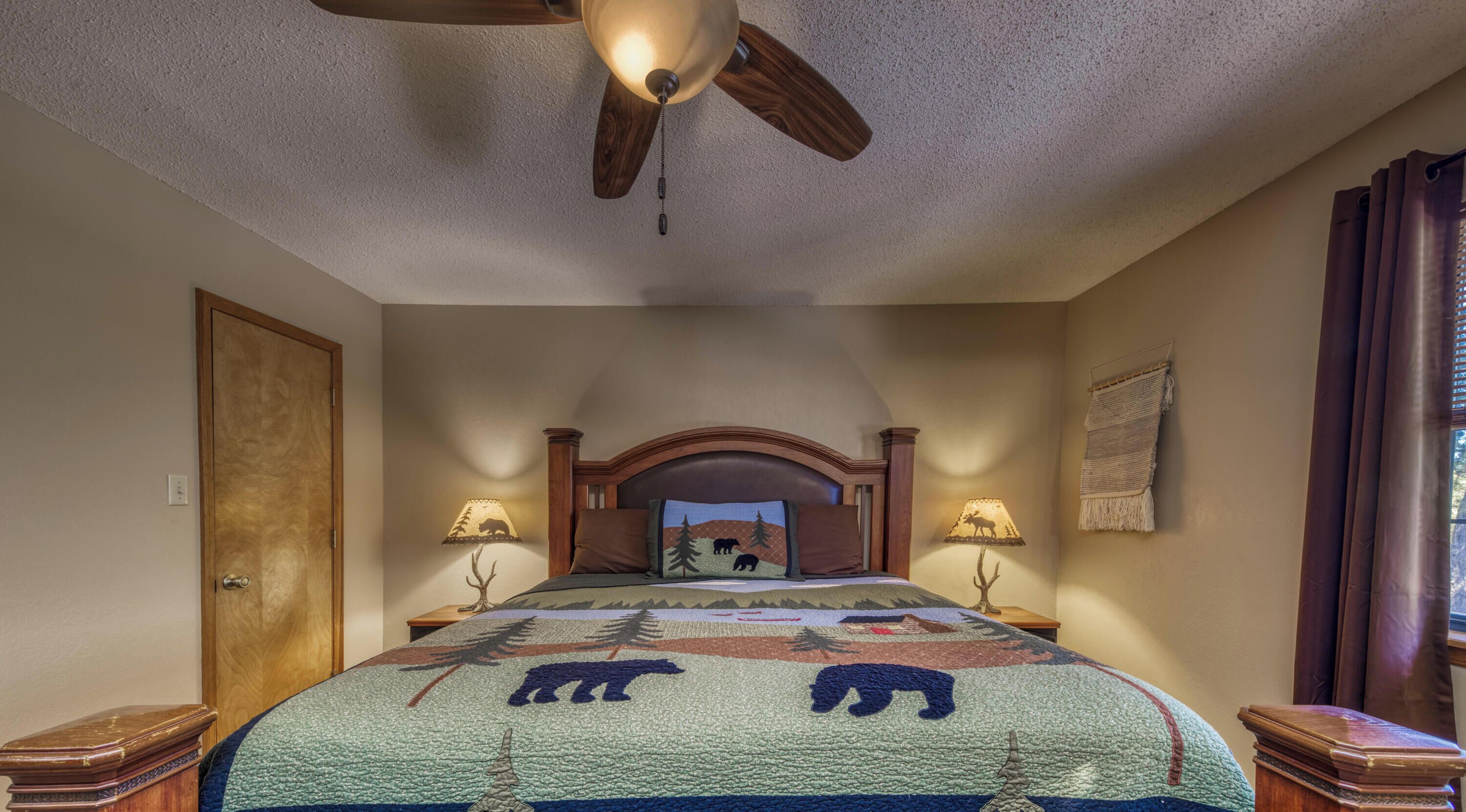 A bedroom with a wooden bed, a ceiling fan, and a view of the outside.