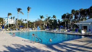 A swimming pool with lounge chairs and umbrellas, surrounded by palm trees and a building in the background. - Ocean Front 2/2 Condo,OCEAN FRONT/MARINA VIEW,Tavernier/Key Largo Fl. Fla.Keys (Tavernier)